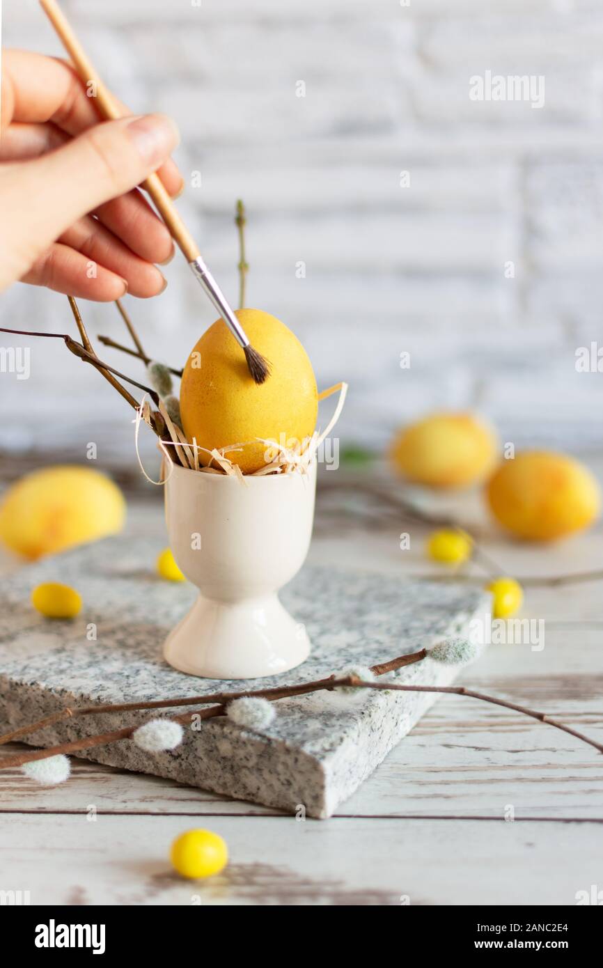 Woman hand paint Easter egg with paintbrush in modern matte yellow color on wooden table. Happy Easter time. Creative Easter decoration. Copy space. Stock Photo