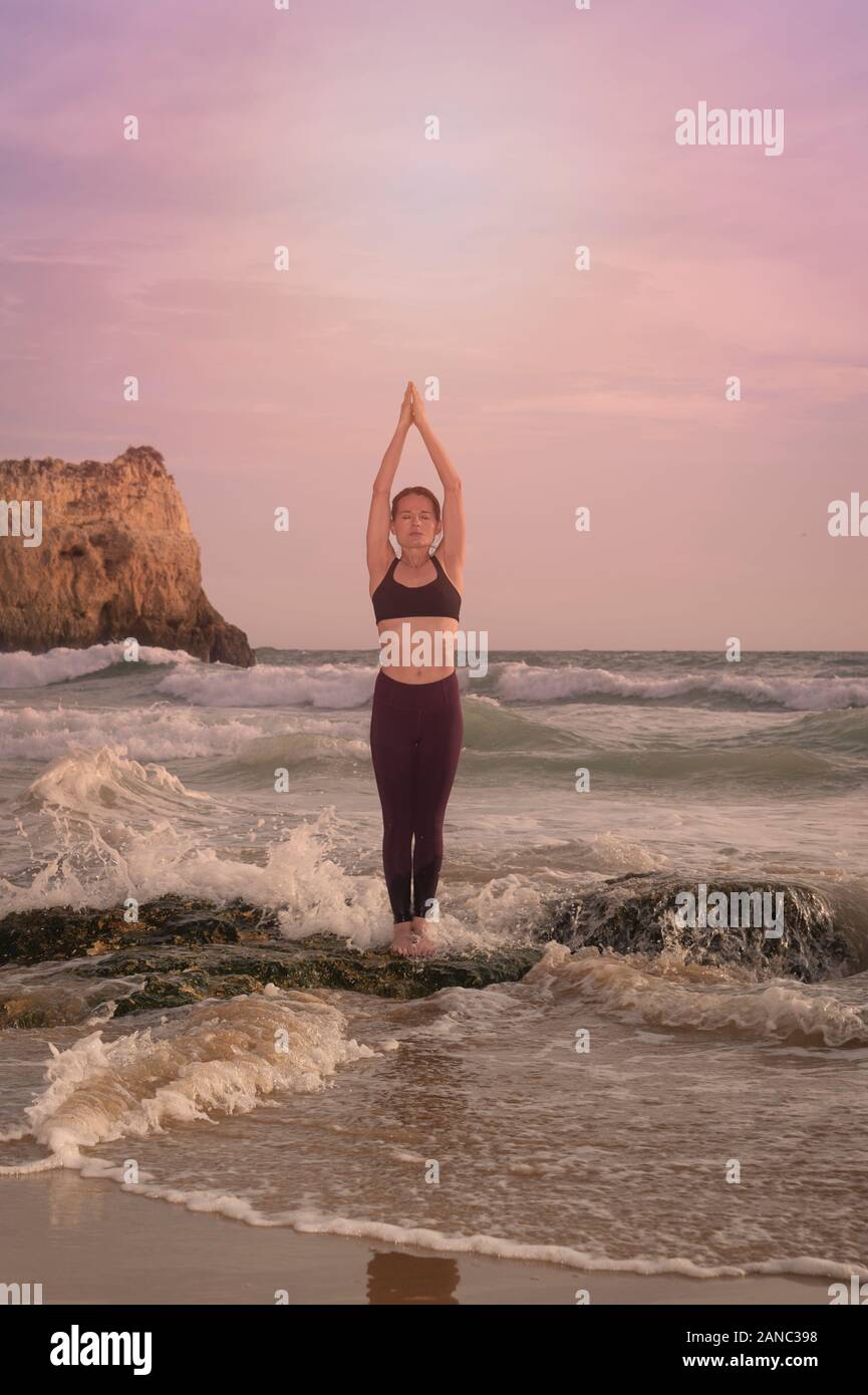 woman standing on a rock by the sea practicing yoga and pilates Stock Photo