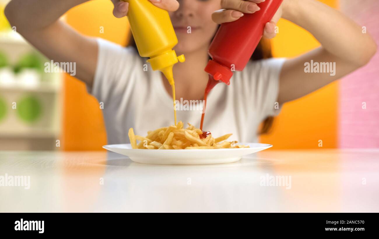 Smiling lady pouring ketchup and mustard on french fries plate