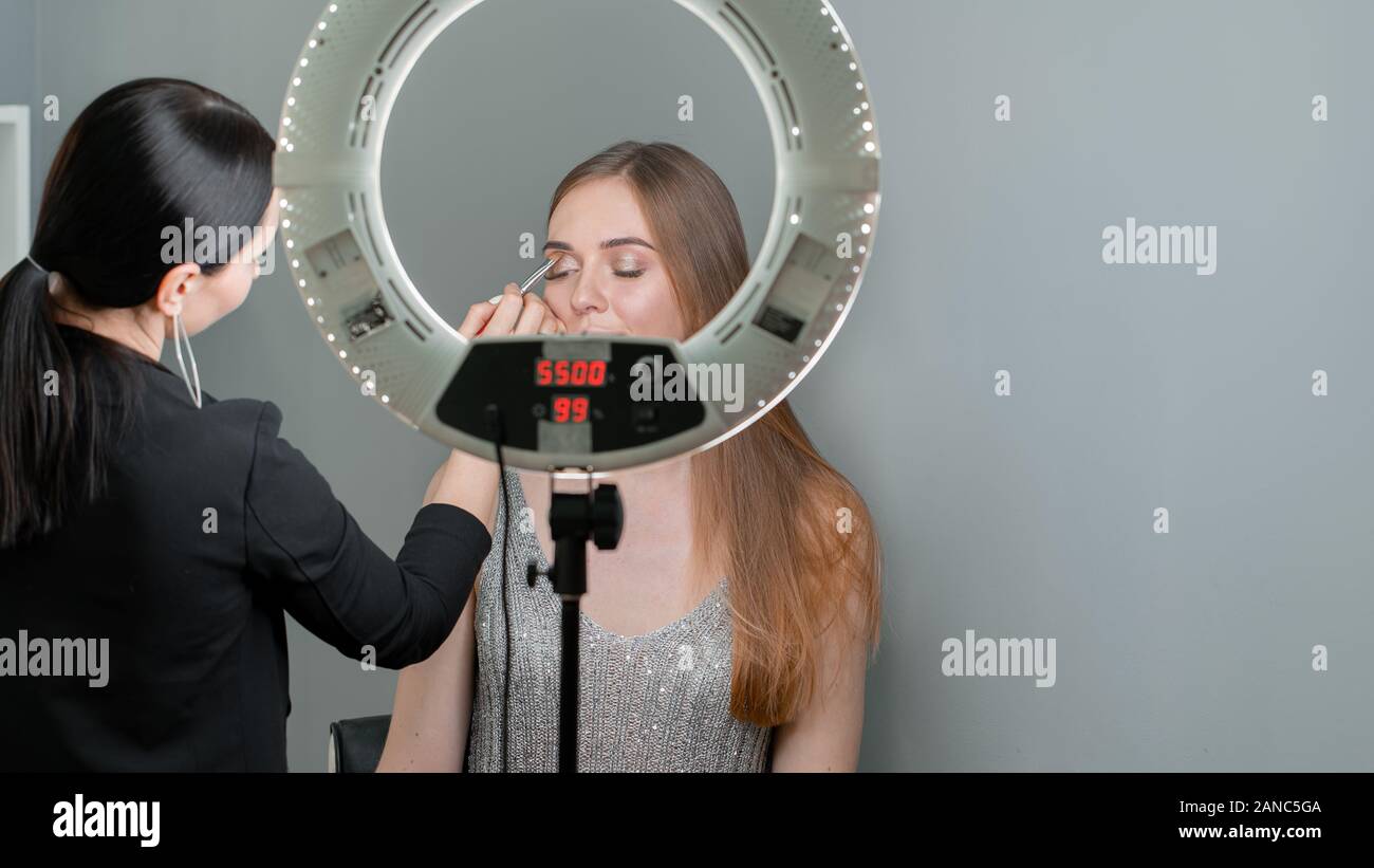 Make-up artist doing makeup to the woman with blue eyes by brush and eye shadow Stock Photo