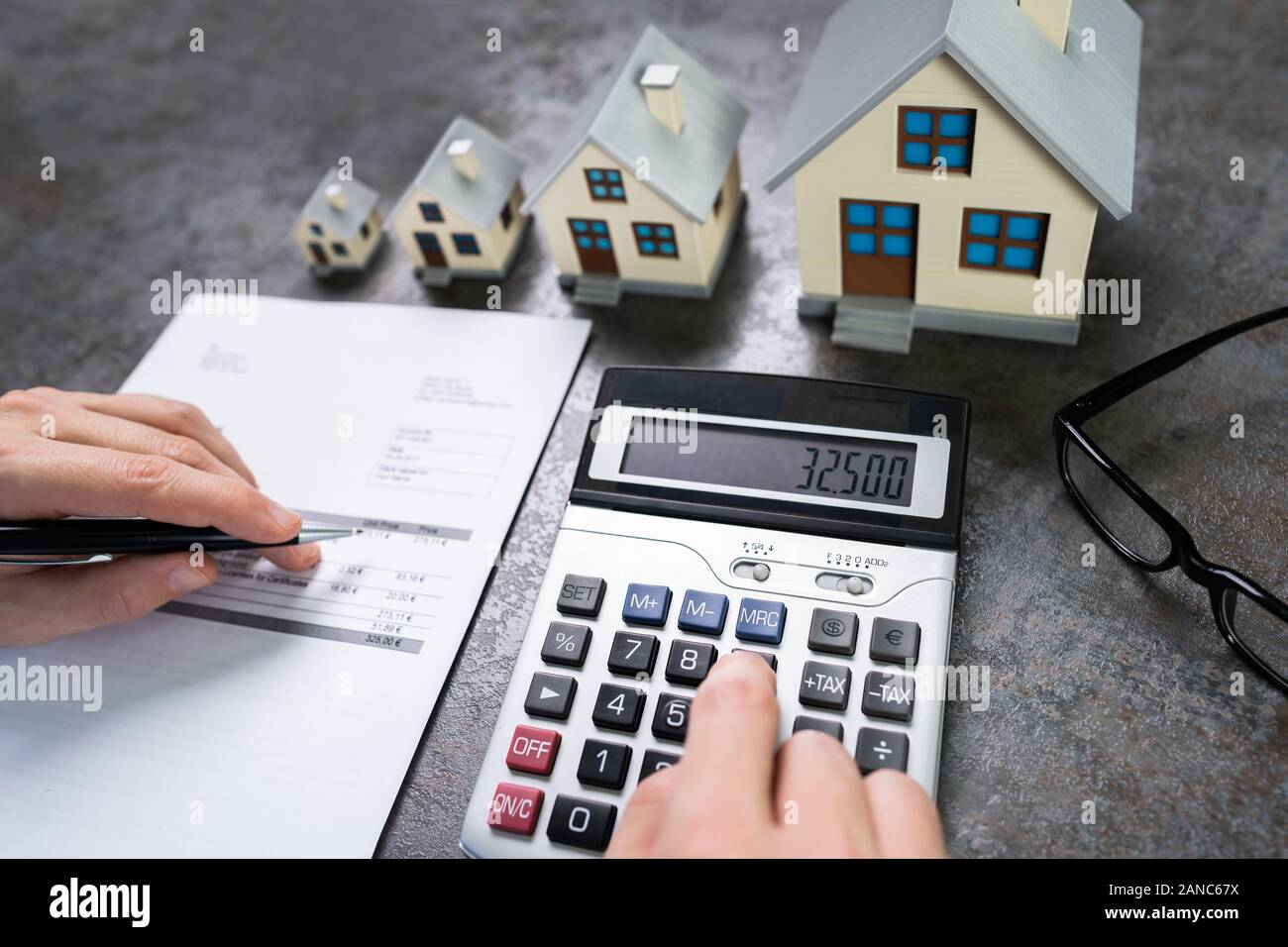 Businessman Calculating Tax By Small And Big House Models Stock Photo