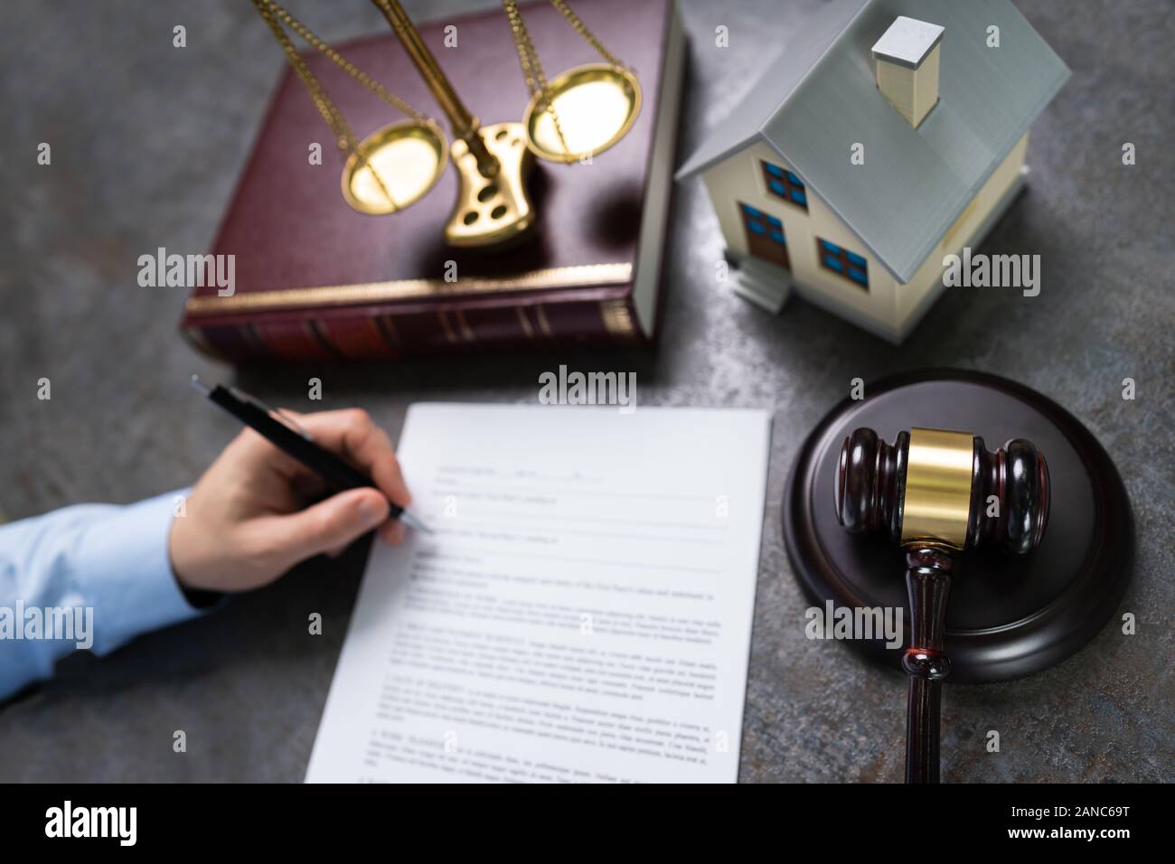Close-up Of Judge With House Model And Gavel Writing On Paper At Desk Stock Photo