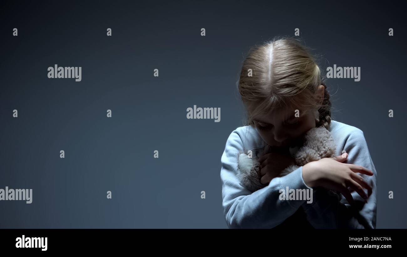 Lonely little child hugging teddy bear, bullying concept, dark background Stock Photo