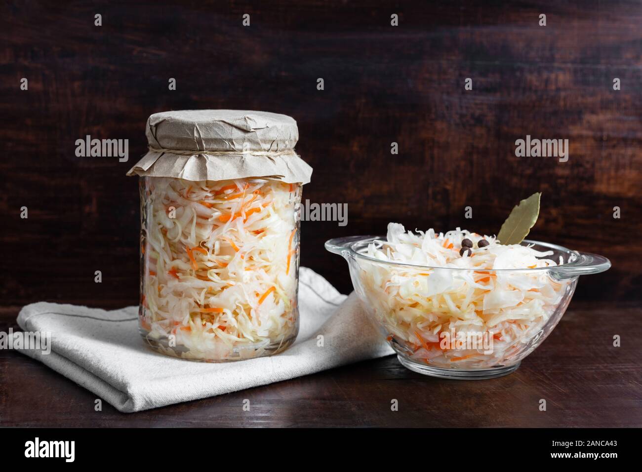 Homemade sauerkraut with carrots in a glass jar and bowl on a dark wooden background. Fermented food. Marinated vegetables. Stock Photo