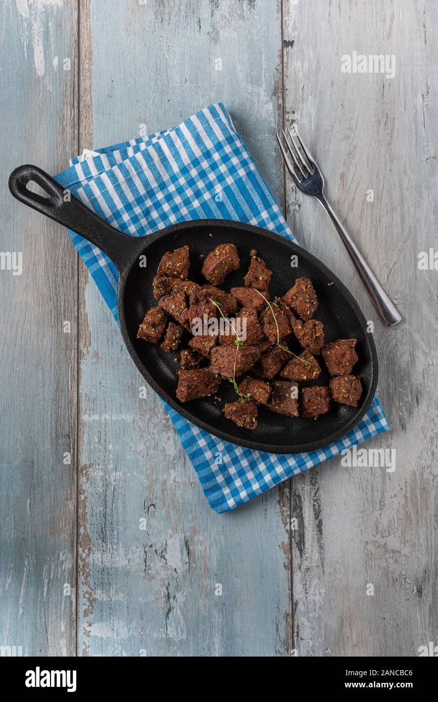 Fried liver cubes in black griddle on wooden background Stock Photo