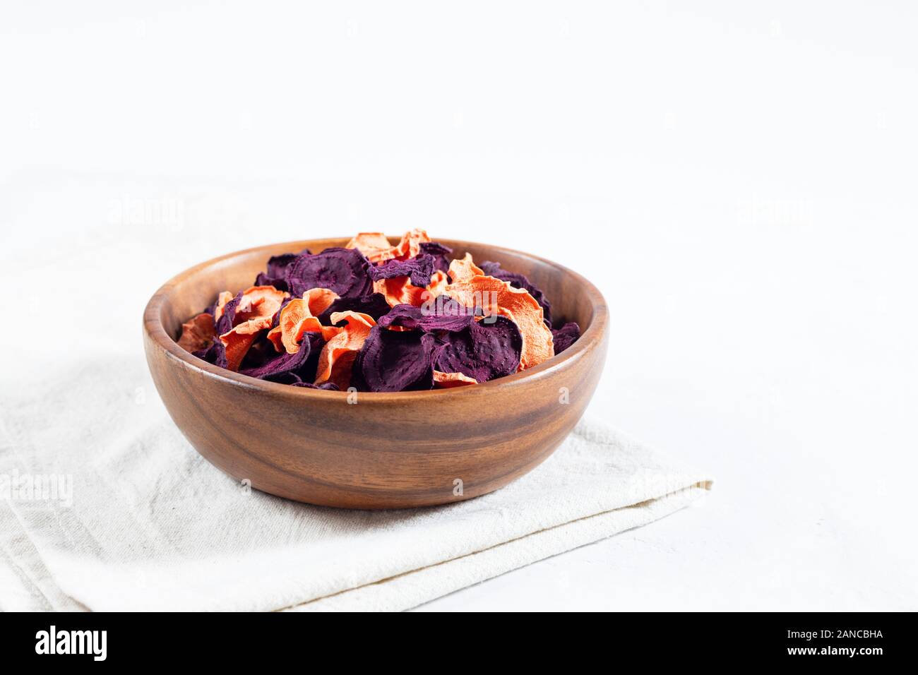Dried carrot and beet chips in a wooden bowl and raw carrots, beets on a white concrete background. Organic natural food. Copy space. Stock Photo