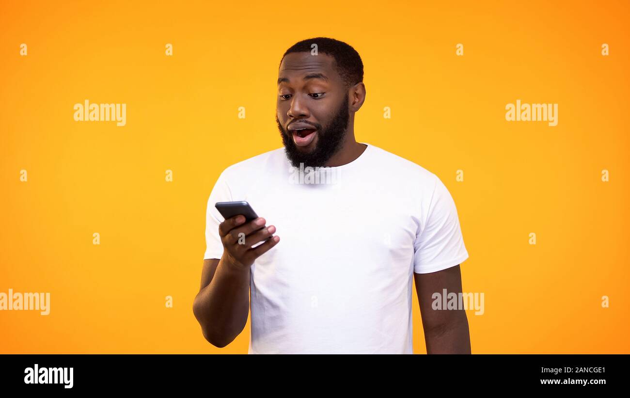 Surprised black man using smartphone application against yellow background Stock Photo