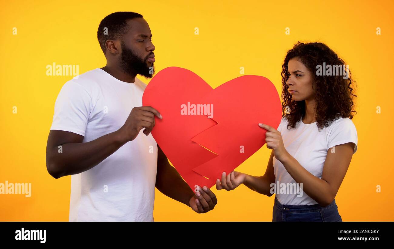 Offended boyfriend and girlfriend holding paper heart parts, relations conflict Stock Photo