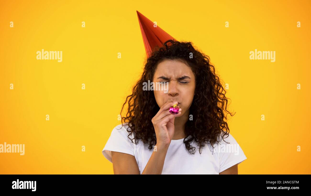Black woman in party hat blowing noisemaker, celebrating birthday