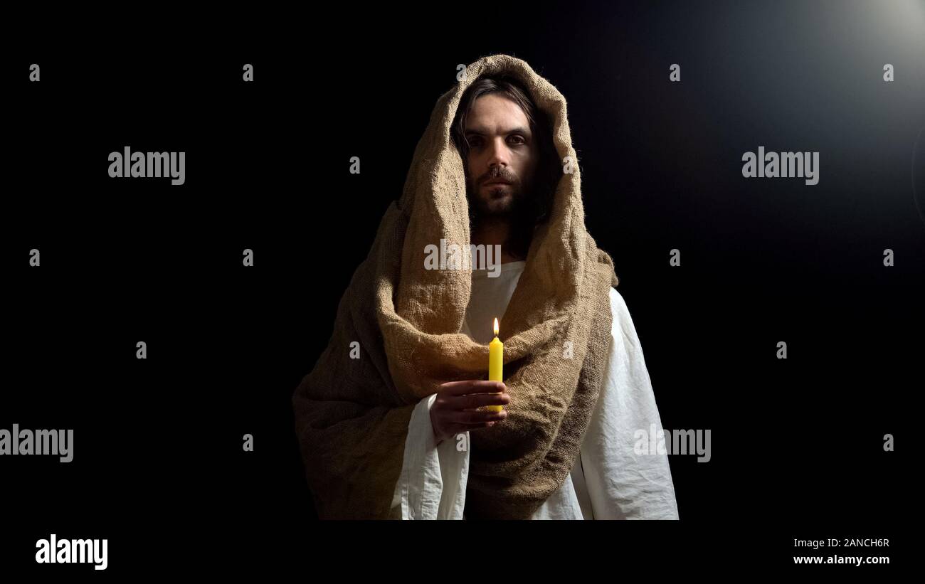 Jesus holding candle, praying for people sins expiation, belief and kindness Stock Photo