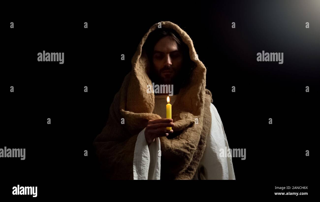 Saint man holding candle, praying for people sins expiation, belief and kindness Stock Photo