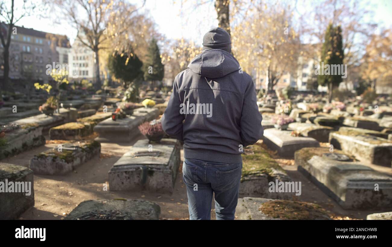 Sad man walking on ancient cemetery, visiting relative, commemorating ancestors Stock Photo
