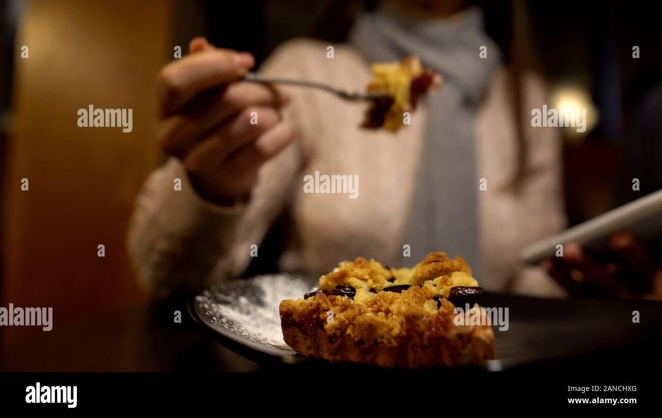 Young lady eating tasty pie and using smartphone, enjoying lunch time alone Stock Photo