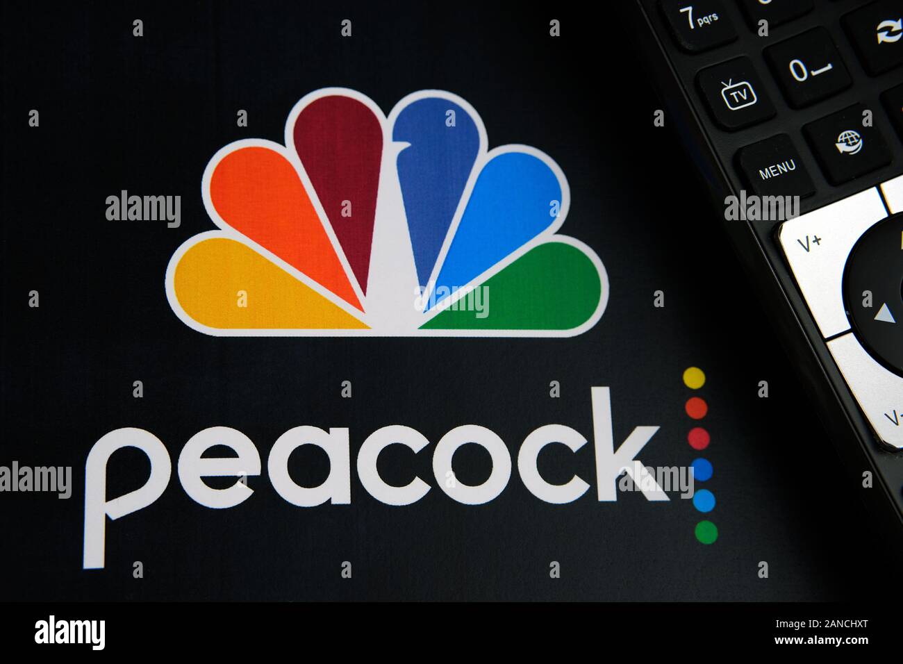Peacock video streaming service logo on the paper brochure and the remote control next to it. By NBCUniversal, a subsidiary of Comcast. Stock Photo