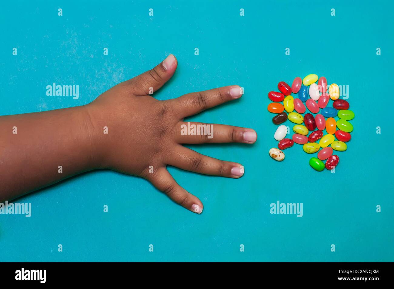 A kids arm and hand with fingers spread out that is about to grab fruit flavored candy from a small serving. Stock Photo