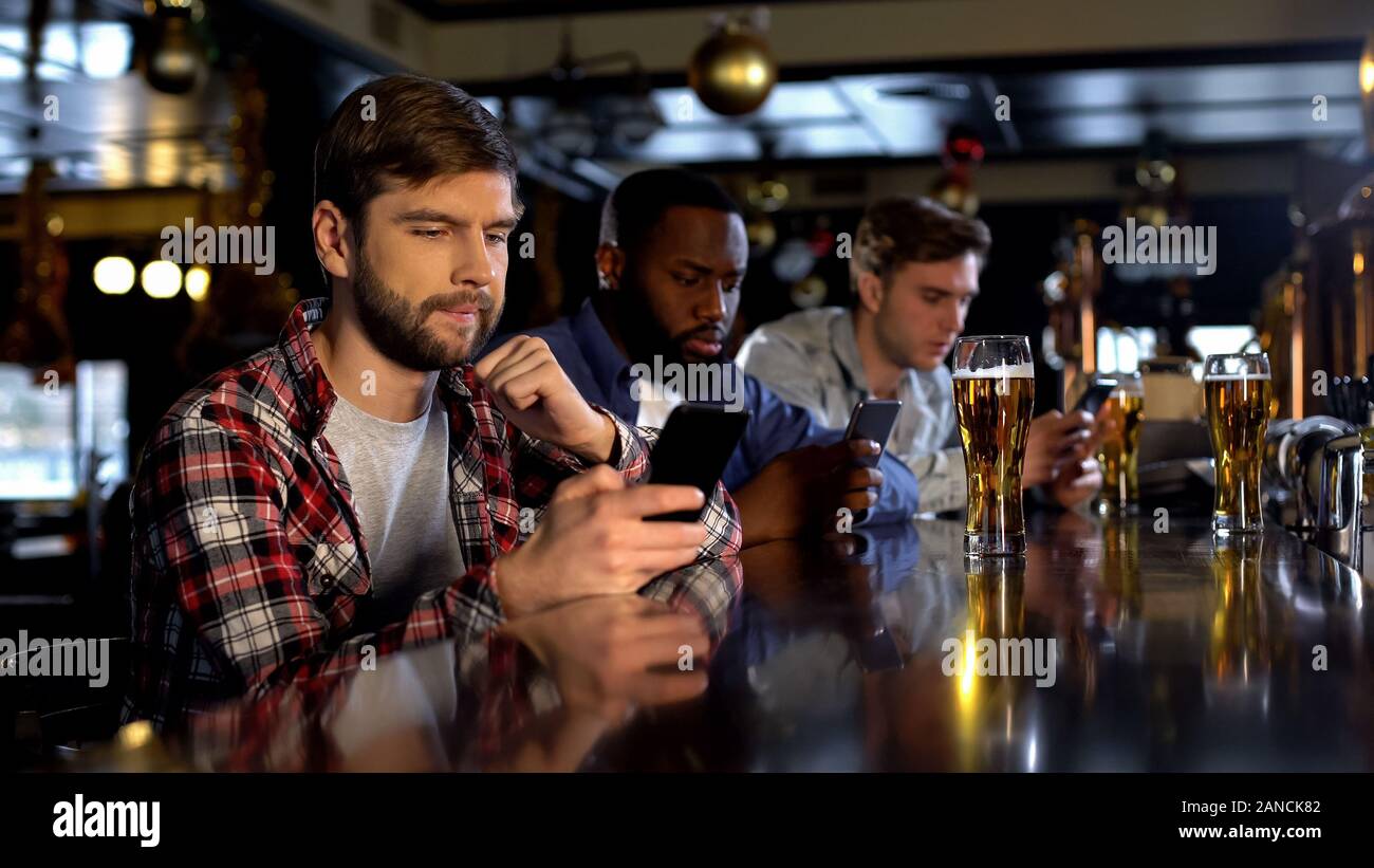 Anxious male fans betting on phone, watching game in pub, gambling application Stock Photo