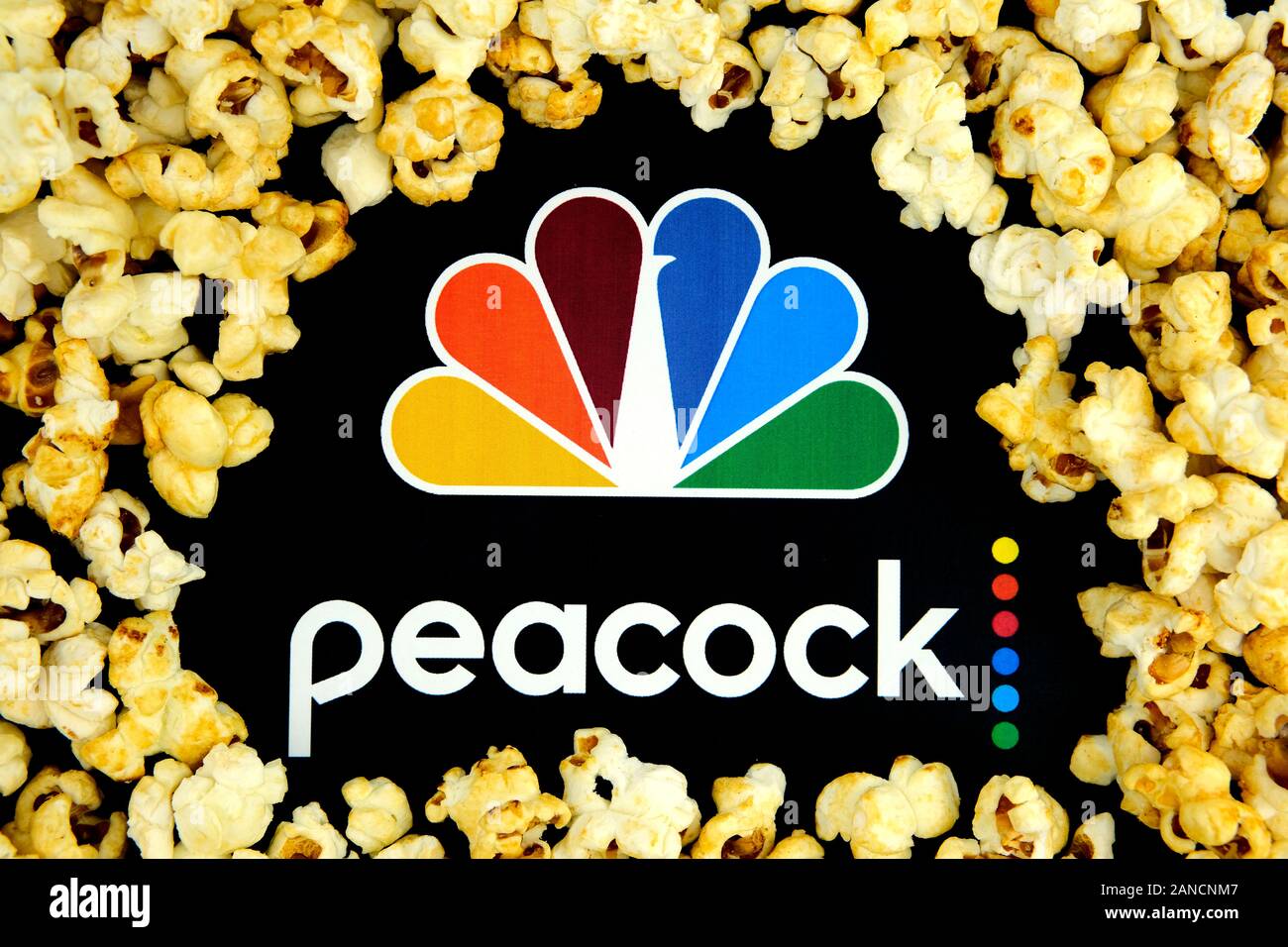 Peacock streaming service logo on the paper brochure and caramel popcorn around it. Concept for a new streaming video service. Stock Photo