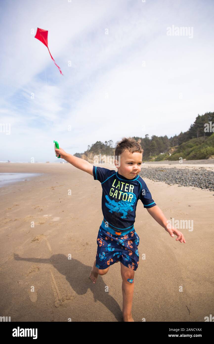 Young boy running kite along the beach with determination. Stock Photo
