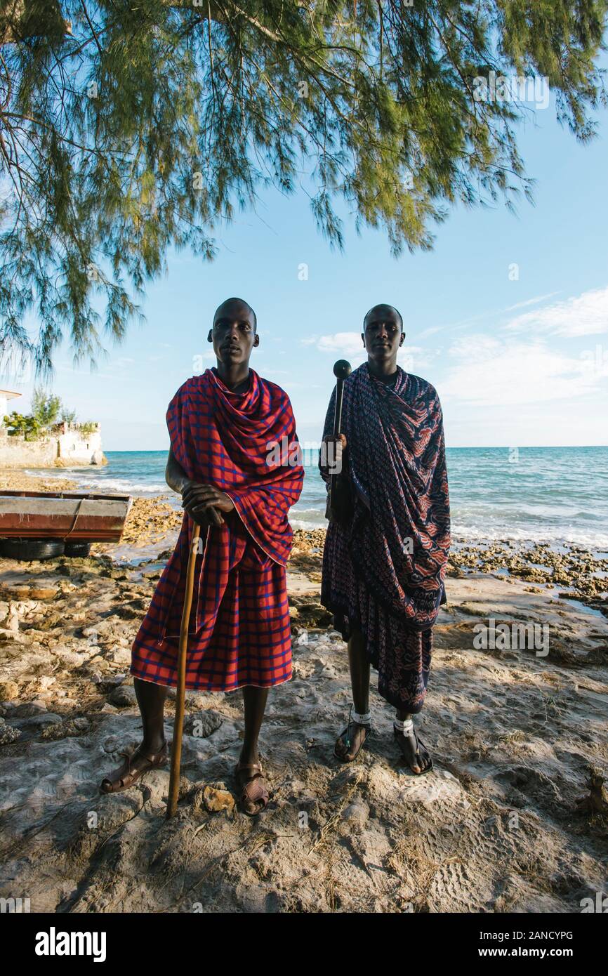 Two masai men in traditional clothes standing on the beach at sunset Stock Photo