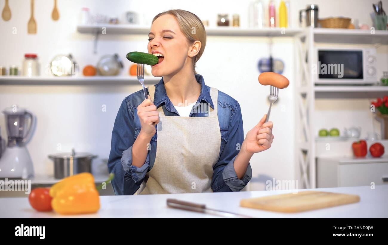 Pretty girl choosing cucumber instead sausage, low-calorie food vs carbohydrates Stock Photo