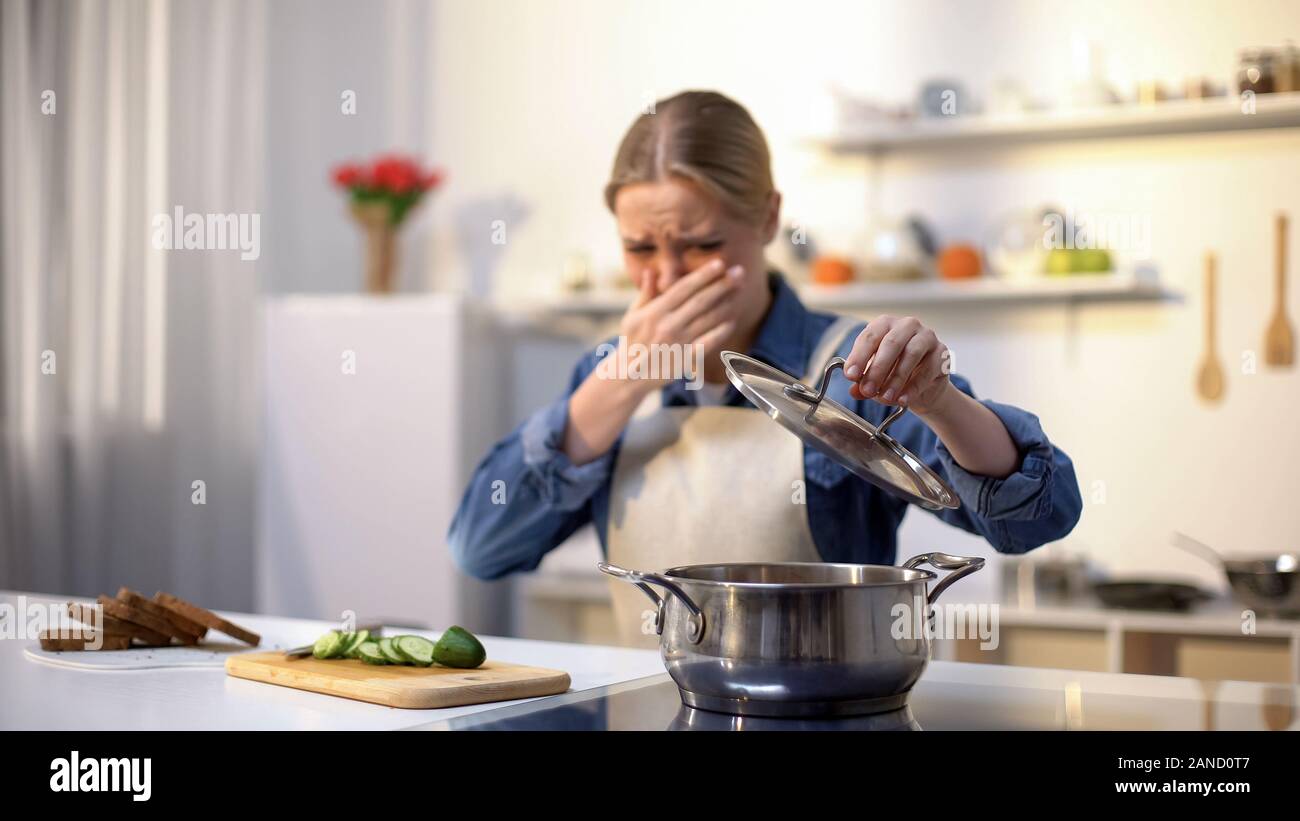 Young woman smelling cooked soup with disgusted face expression ...
