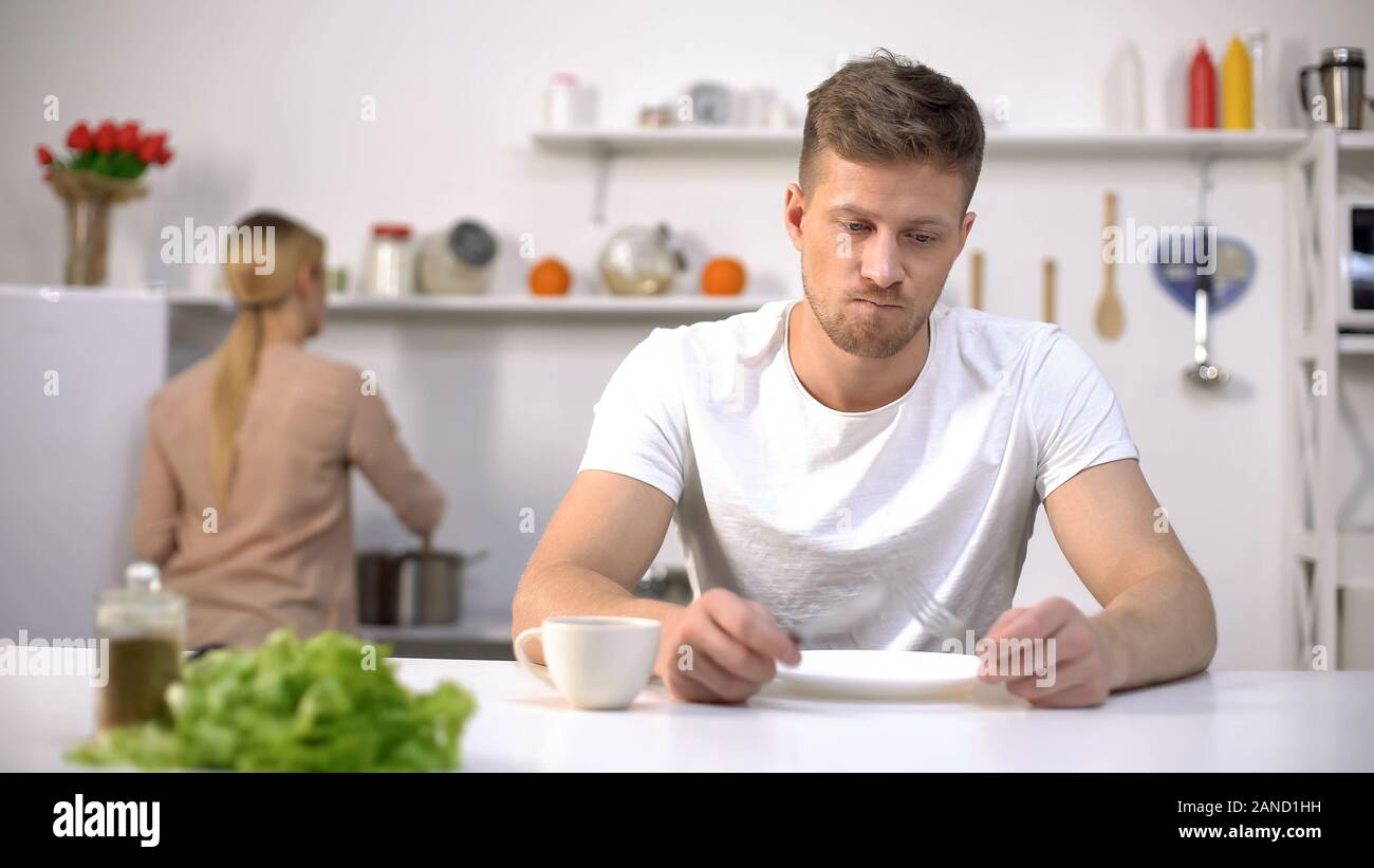 Hungry man eagerly waiting for dinner, wife cooking on background, starvation Stock Photo