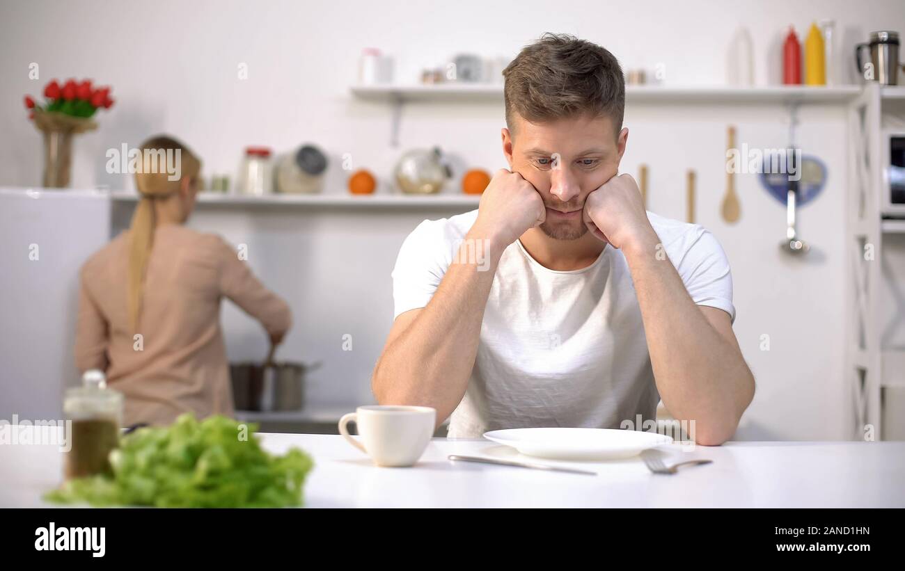 Upset hungry man waiting for dinner, wife cooking on background, divorce risk Stock Photo