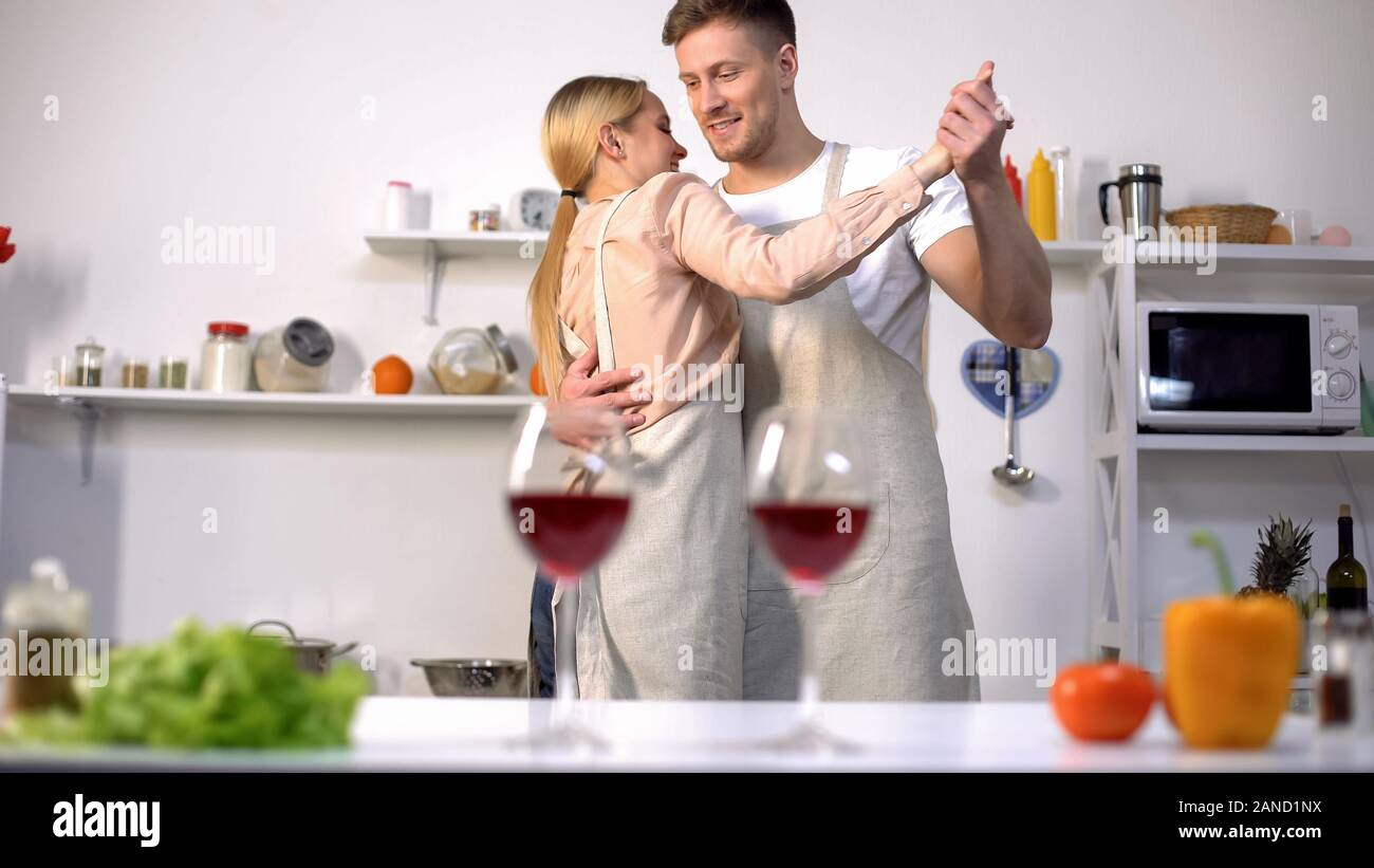 Glasses of red wine on table, romantic couple dancing on background in kitchen Stock Photo