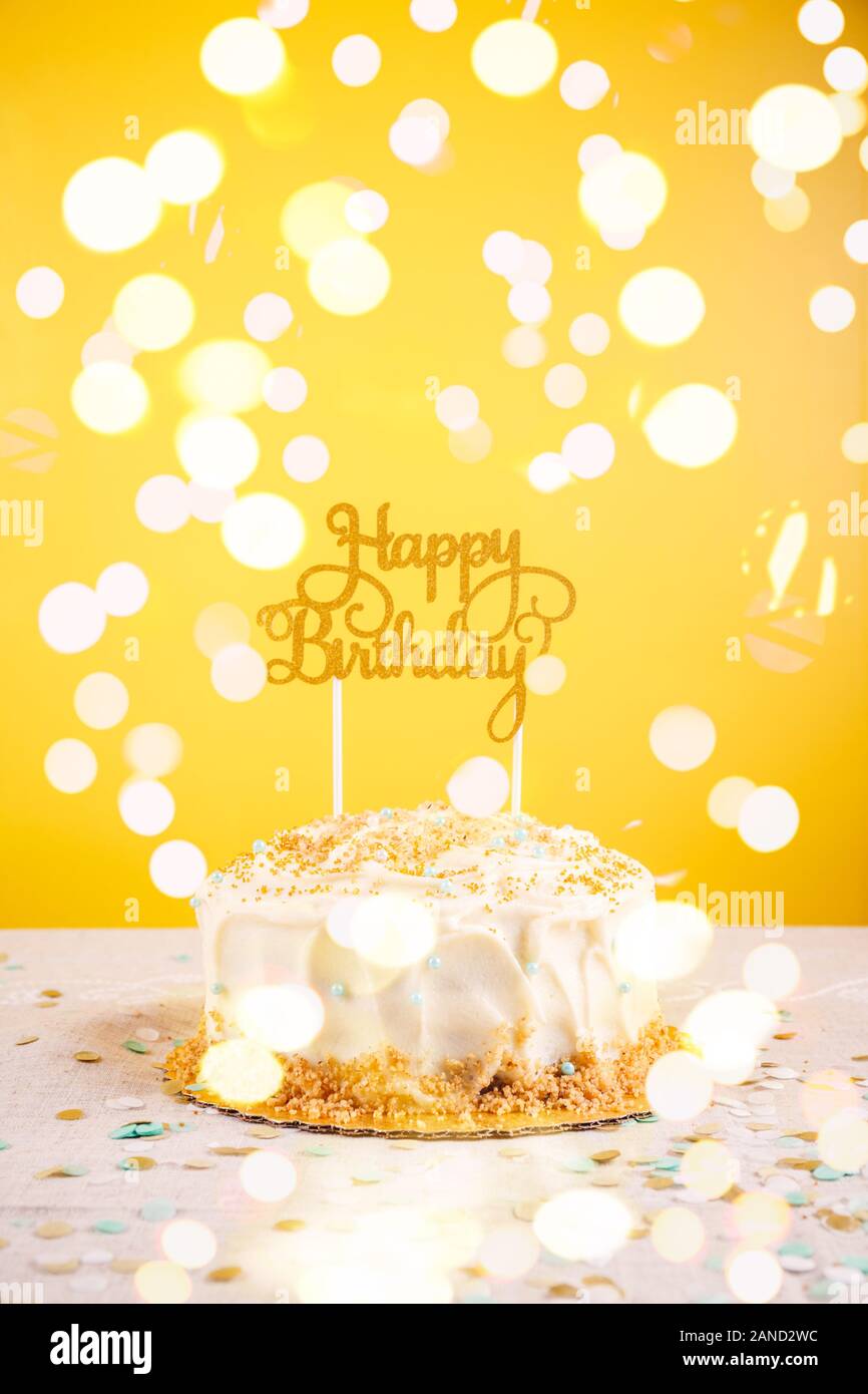 Birthday cake with golden topper. Birthday party celebration concept. Vertical, bold yellow background, bright lights bokeh background Stock Photo