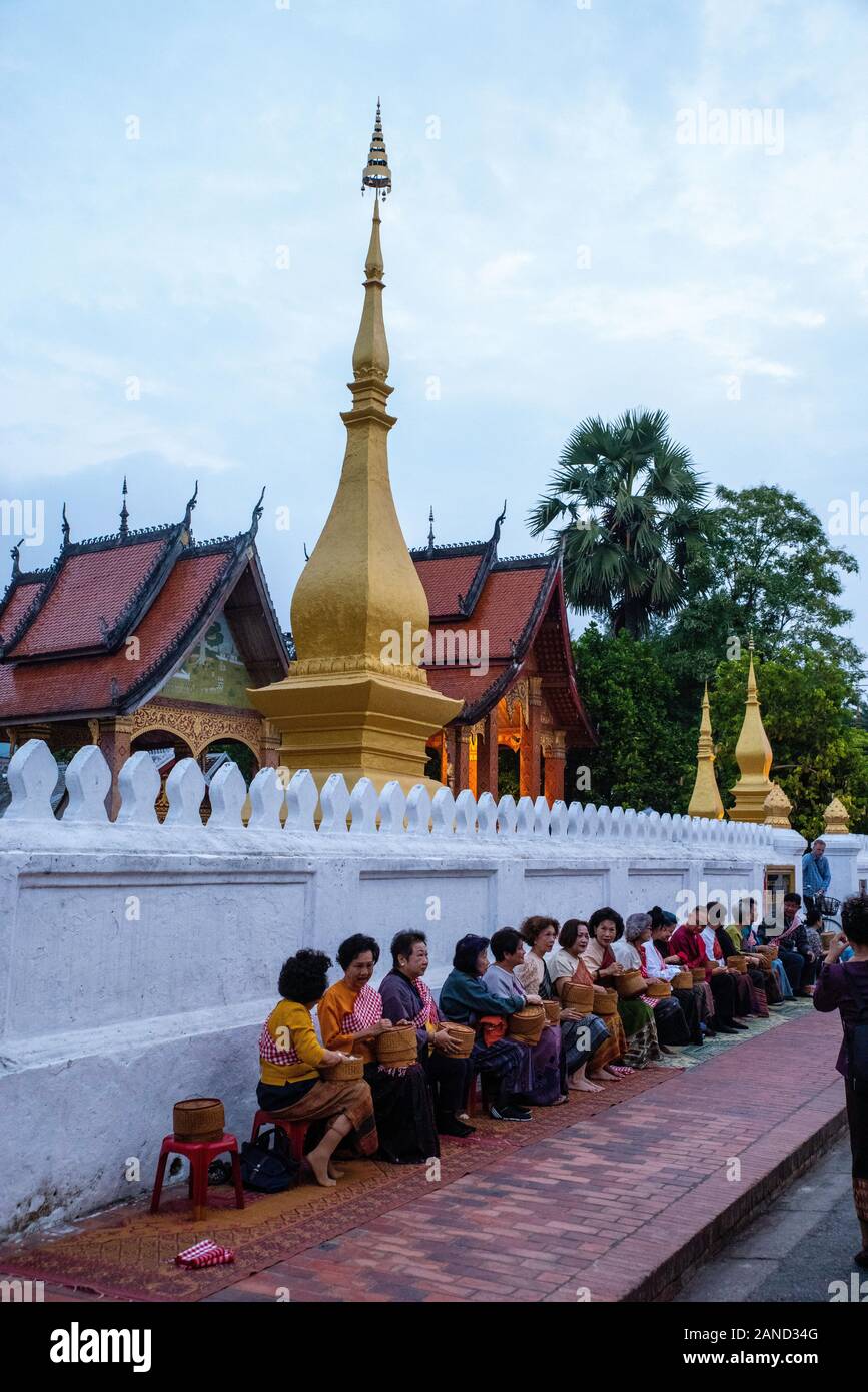 Monks and tourists participate in sai bat (morning alms giving), Wat Sesnsoukharam, Sakkaline Road, Luang Prabang, Laos. Stock Photo