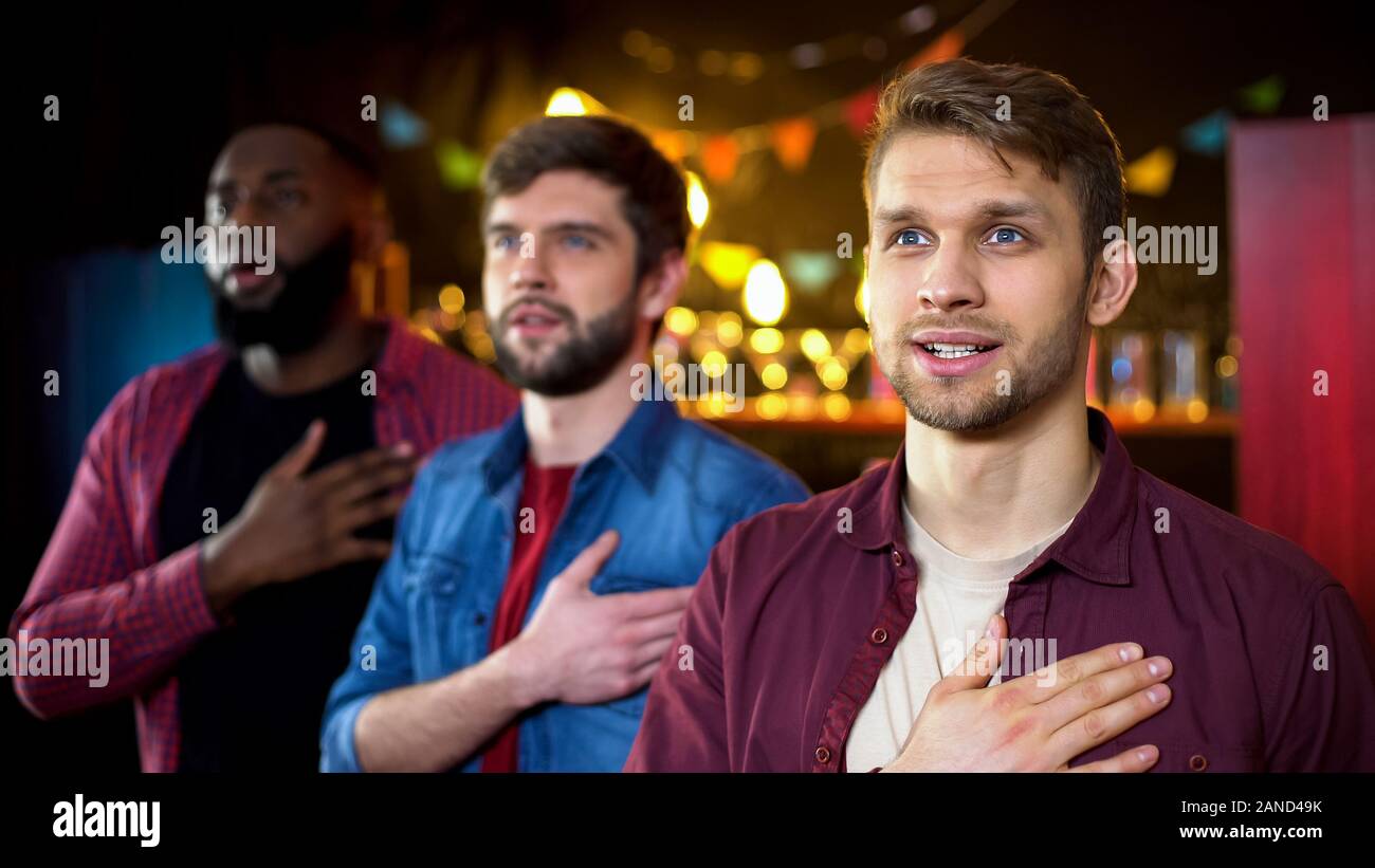 Patriotic football fans listening to national anthem, watching game in bar Stock Photo