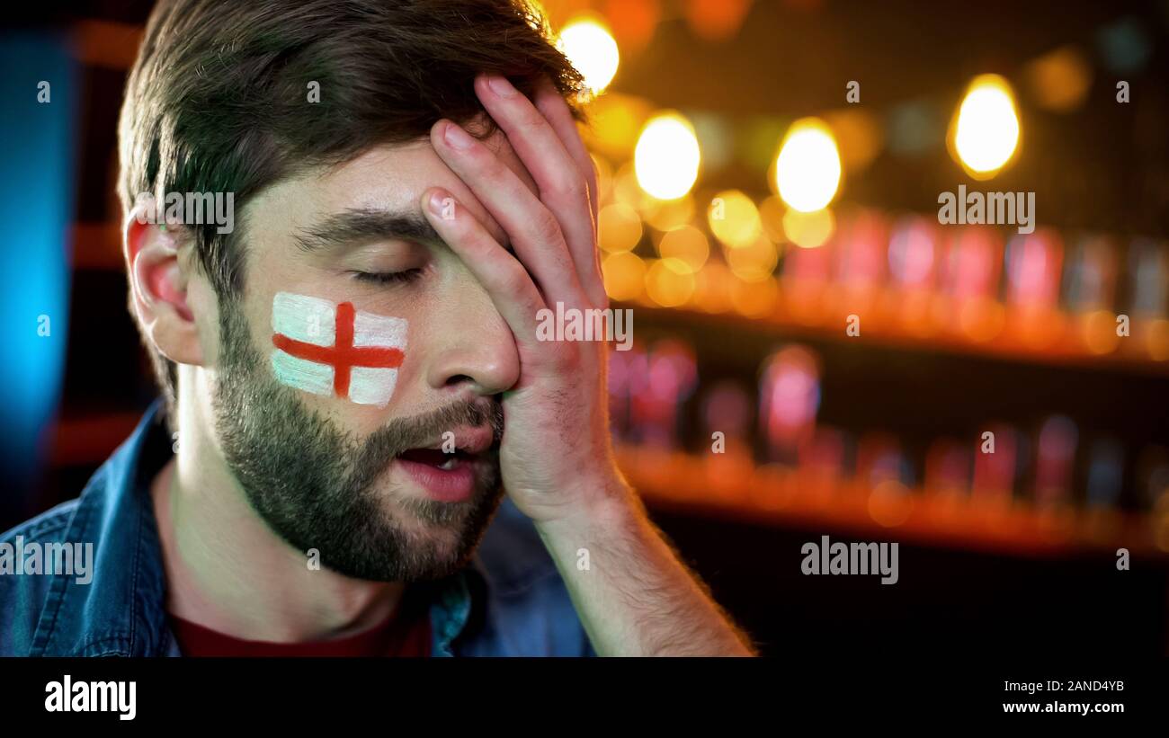 Displeased male football fan with english flag on cheek making facepalm gesture Stock Photo