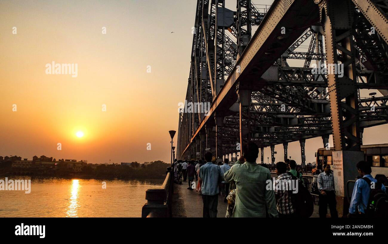 KOLKATA,WEST BENGAL/INDIA-MARCH 20 2018:At Howrah bridge the sun sets as commuters and the public alike cross its busy sidewalk. Stock Photo