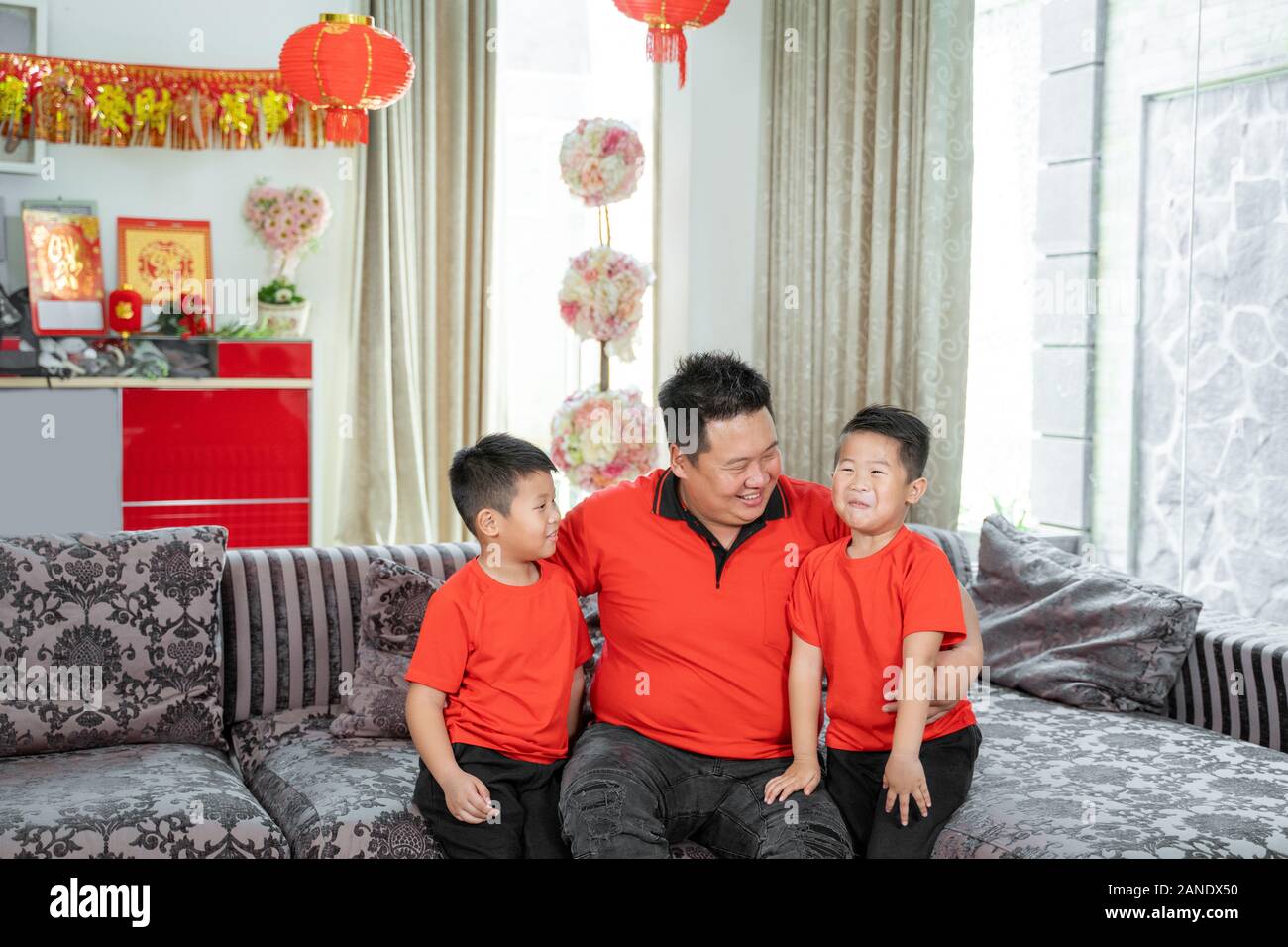 Smiling chinese father and two son wearing red theme clothing sitting on the couch Stock Photo