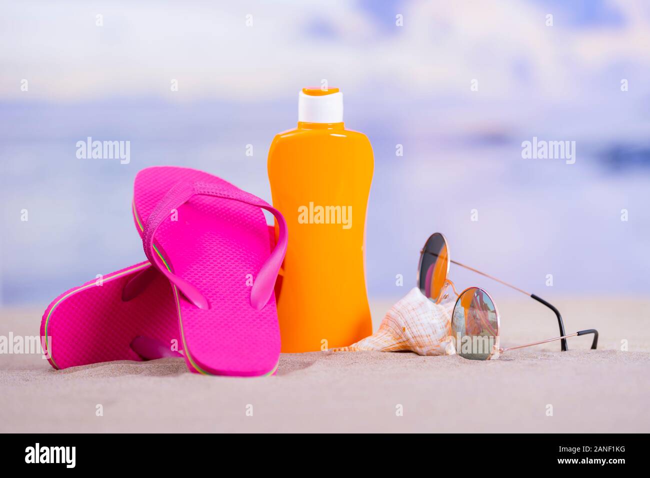 Close-up of an orange sunscreen bottle surrounded by pink flip flops and a  pair of