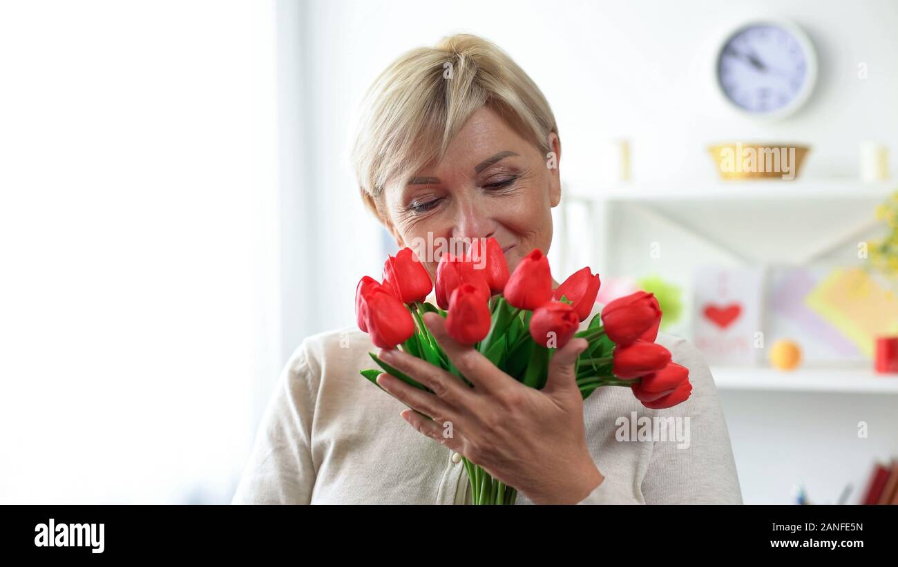 Senior blond lady sniffing tulips bouquet, holiday present from relatives, gift Stock Photo