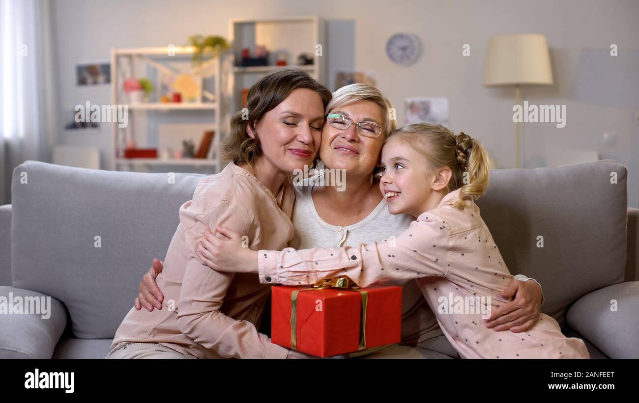 Females hugging granny holding gift box, present from daughter and granddaughter Stock Photo