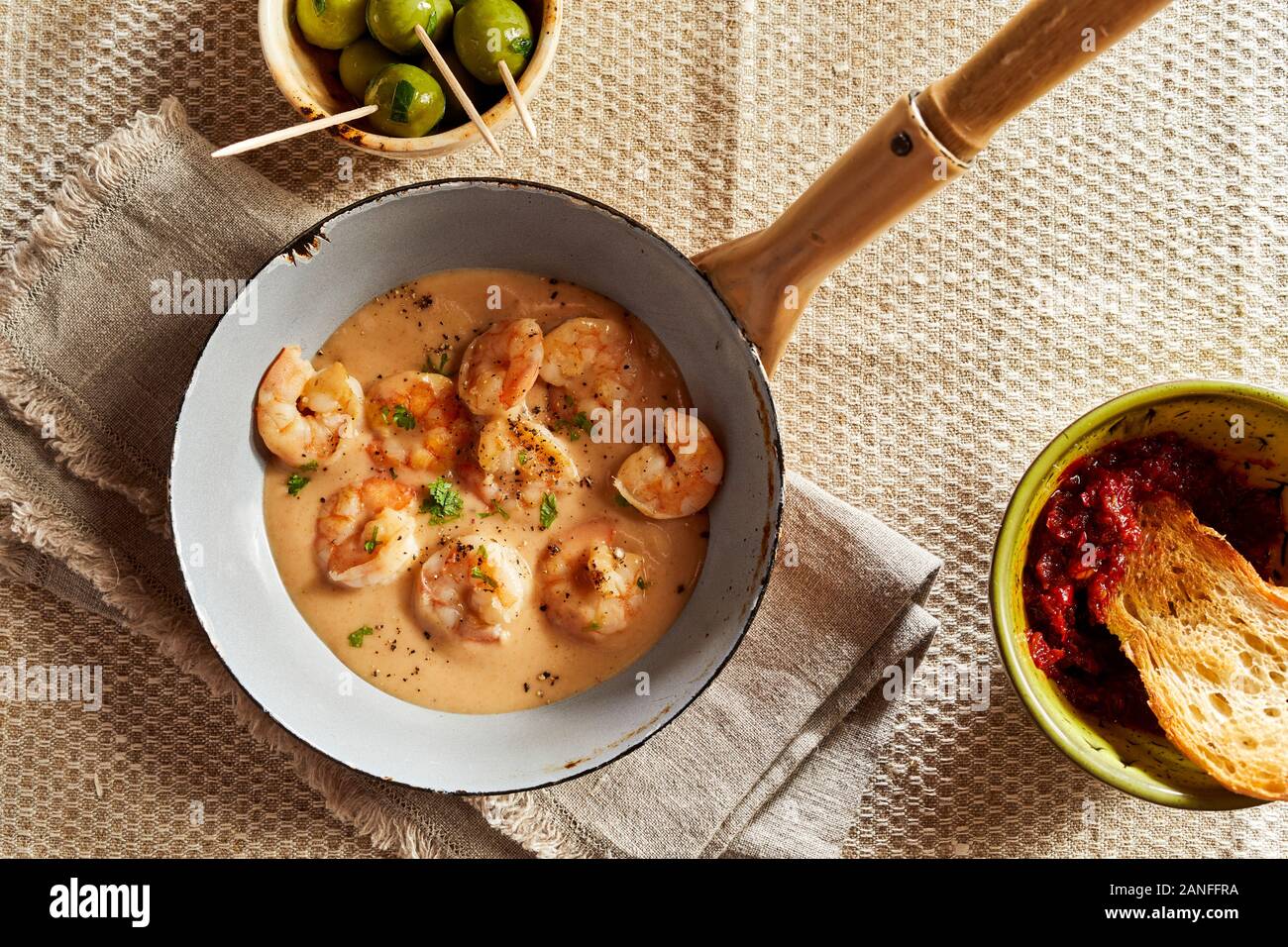 Scampi lobsters in cheese-cream sauce or kase sahne sauce served in pan on rustic restaurant style, with bowl of olives and white bread in sauce, view Stock Photo