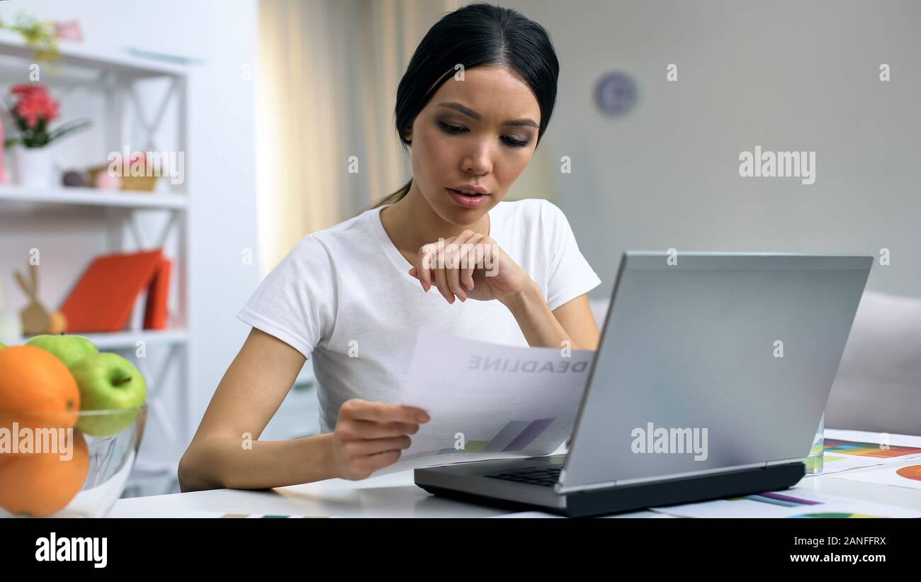 Freelance designer holding document working laptop at home, workload deadline Stock Photo