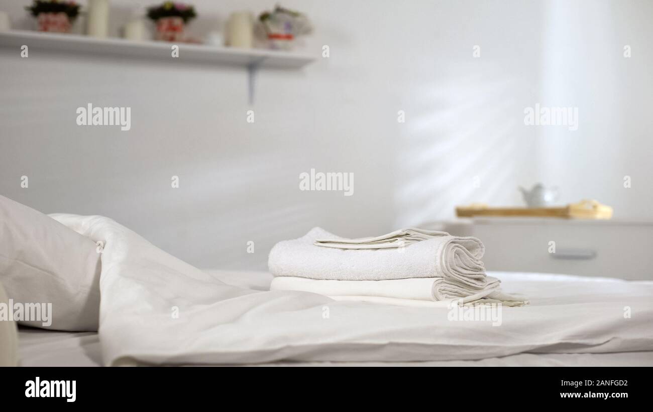 Fresh towels lying on clean bed in hotel room, fragrant fabric softener gel Stock Photo