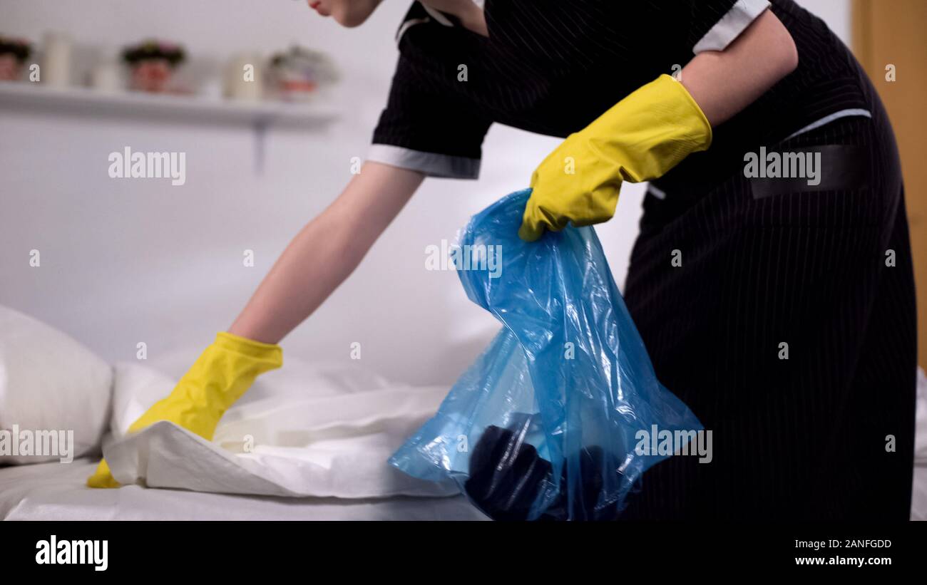 Chambermaid gathering trash from bed in morning after party, cleaning service Stock Photo