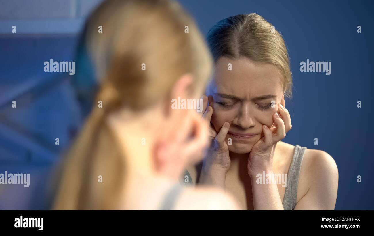 Deeply upset young woman looking sadly mirror, unhappy with appearance, puberty Stock Photo