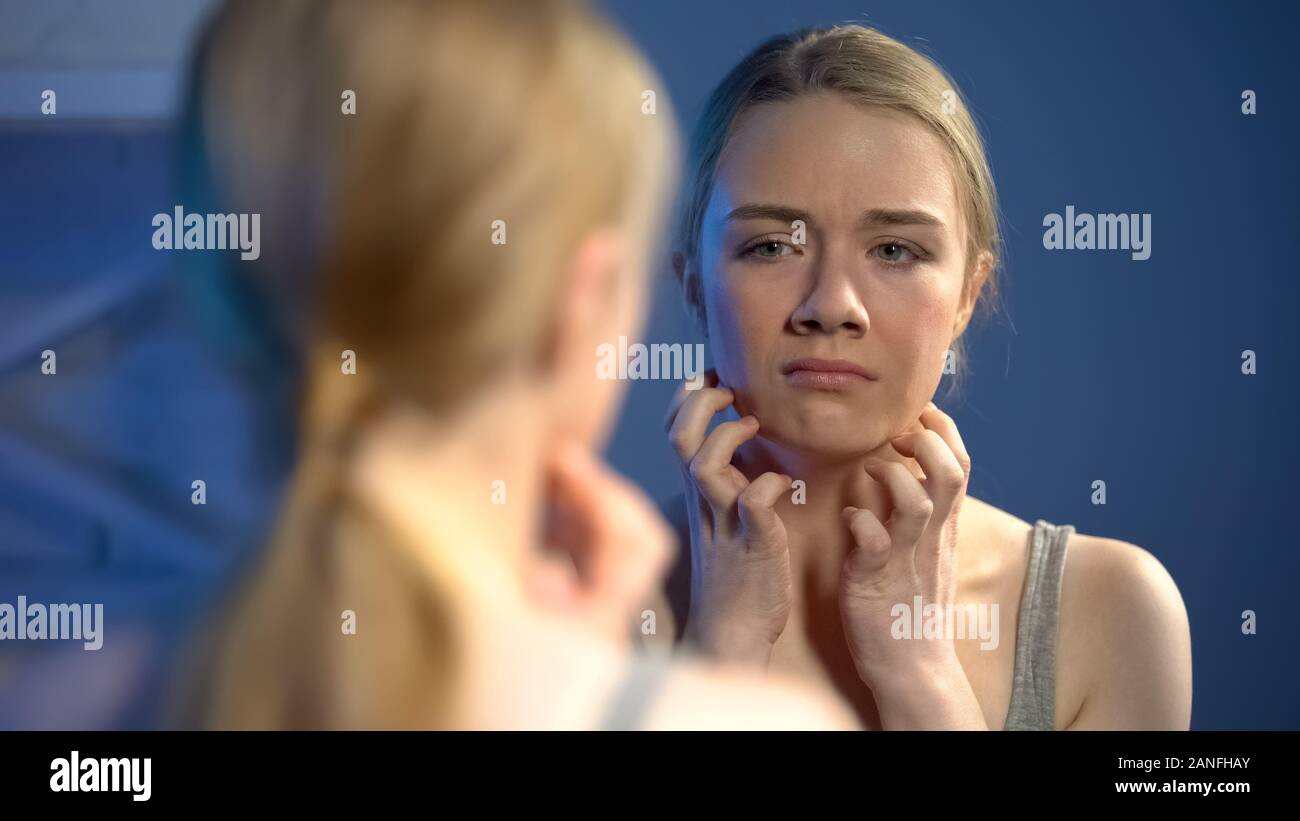 Unhappy young lady looking in mirror reflection, upset with skin imperfection Stock Photo