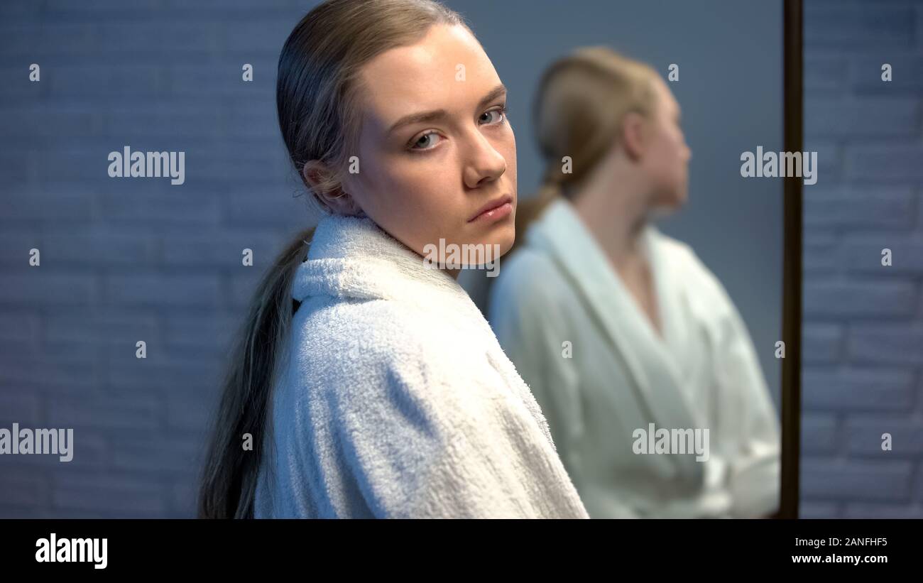 Upset teen girl looking sadly to camera, standing in front of mirror, need help Stock Photo