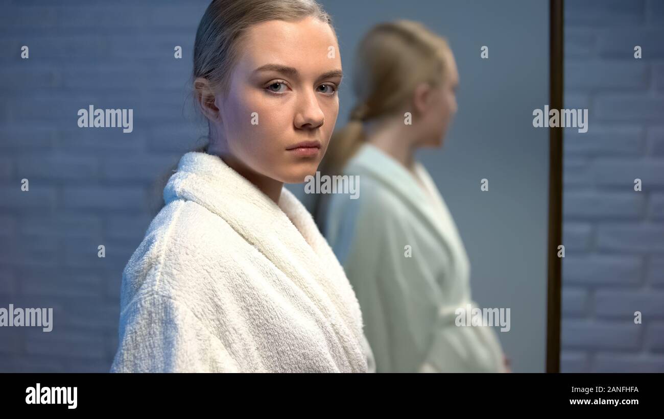 Pensive pregnant girl looking to camera in front of mirror, unplanned pregnancy Stock Photo