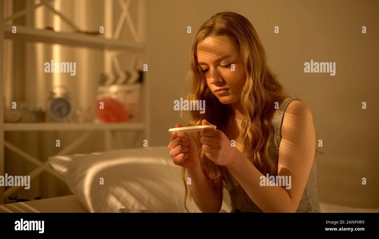 Young woman looking at pregnancy test result in contraception, unplanned child Stock Photo