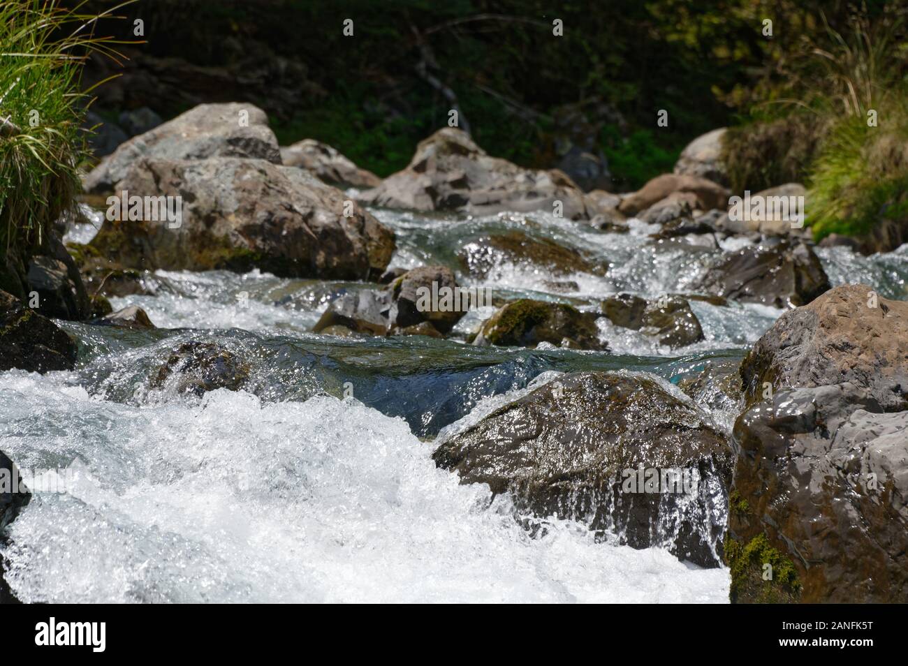 The force of the water creates white water in between boulders in a river Stock Photo