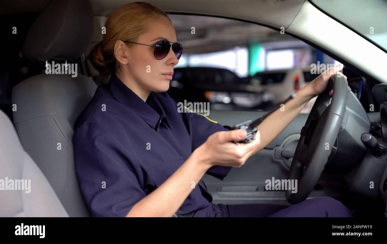 Serious female officer holding radio set and driving car, emergency situation Stock Photo
