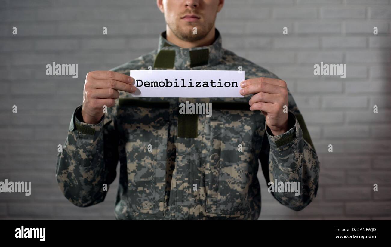 Demobilization word written on sign in hands of male soldier, end of term Stock Photo