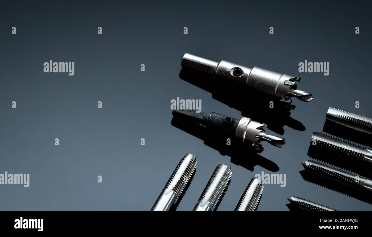 Closeup straight flute tap tip and hole saw on dark background